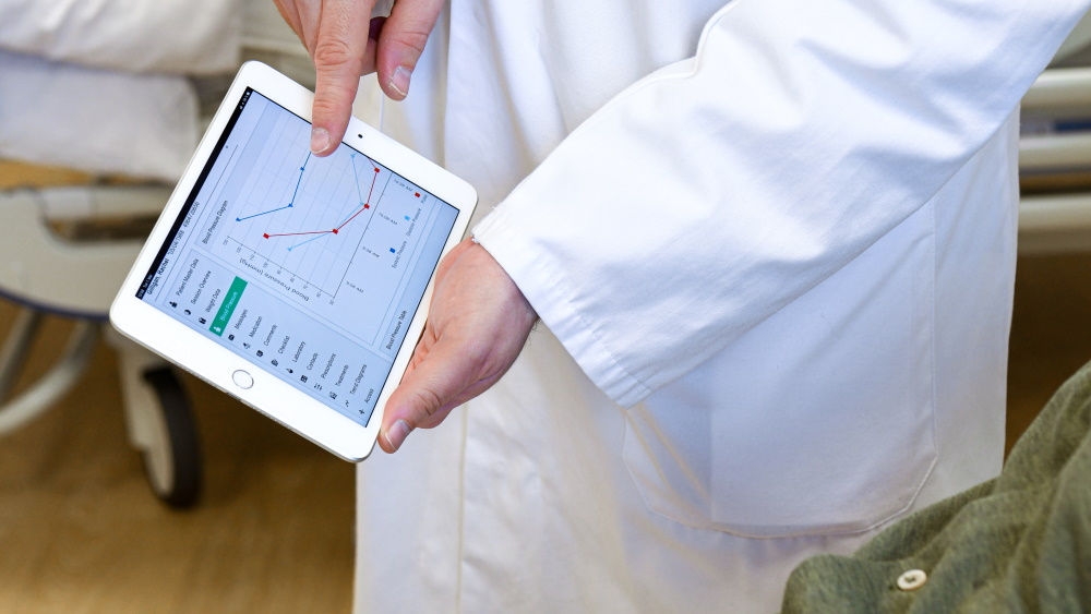 Hände einer medizinischen Fachkraft, die ein Tablet mit geöffnetem NEXADIA® Mobile Companion hält und statistische Daten anzeigt