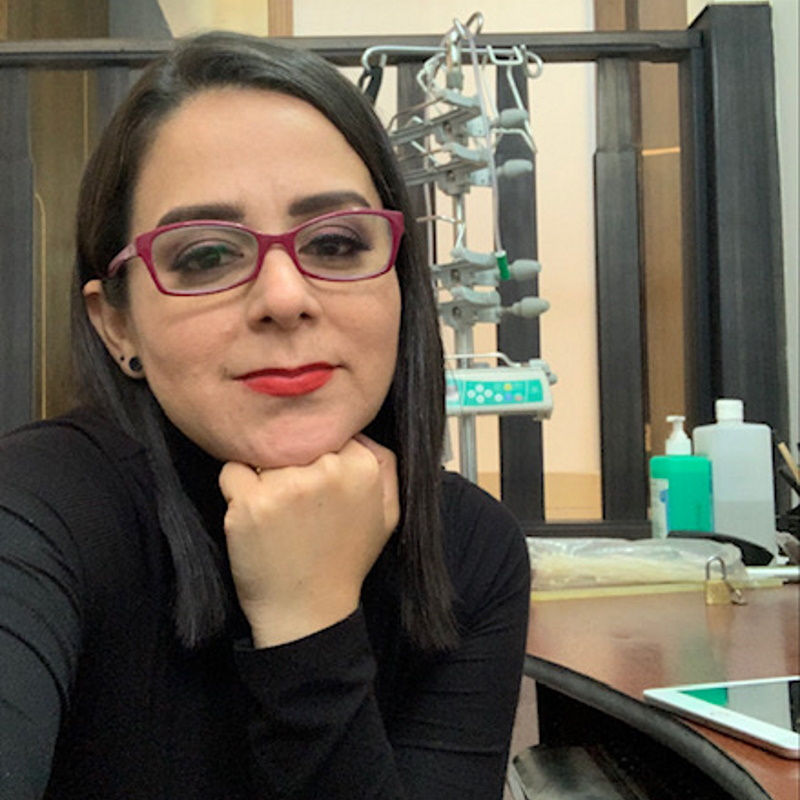 Frau mit dunklen Haaren, Brille und Lippenstift ruht ihren Kopf auf der Hand