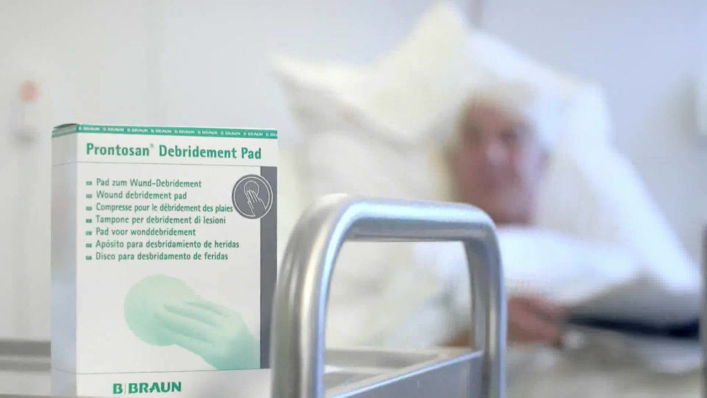 eine Packung Prontosan® Debridement Pad, die im Krankenhauszimmer aufgenommen wurde, im Hintergrund liegt der Patient auf dem Bett