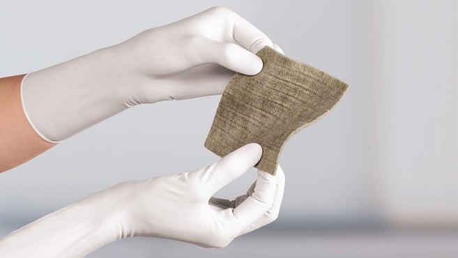 Askina Calgitrol AG+, leicht gewellt, mit zwei Händen in weißen Untersuchungshandschuhen gehalten