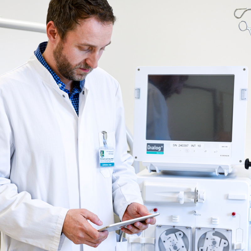 Ein männlicher Arzt steht in der Nähe eines großen Bildschirms eines medizinischen Geräts und arbeitet mit seinem Tablet