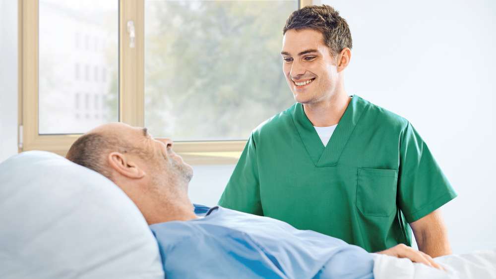Pflegekraft und Patient in einem Krankenhauszimmer, beide lächelnd